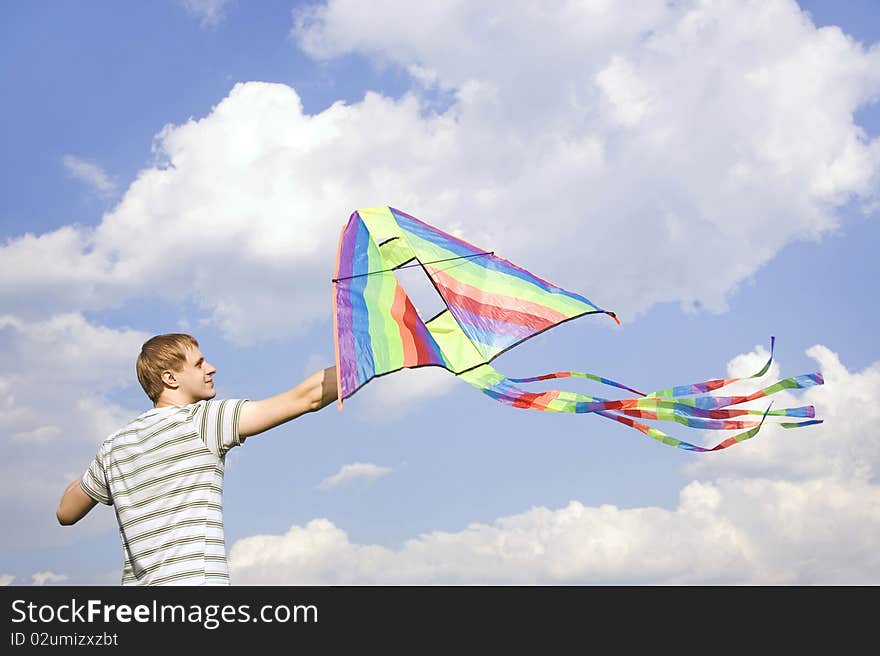 Young man holding multicolored kite and looking on it, summer time