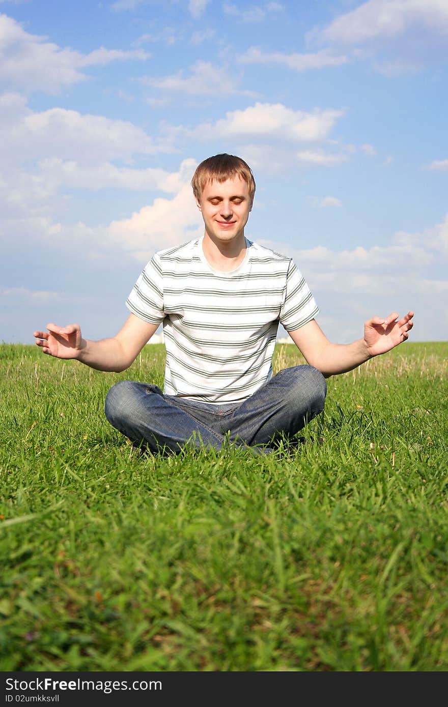 Young handsome man sitting on green summer lawn and meditating with closed eyes. Young handsome man sitting on green summer lawn and meditating with closed eyes