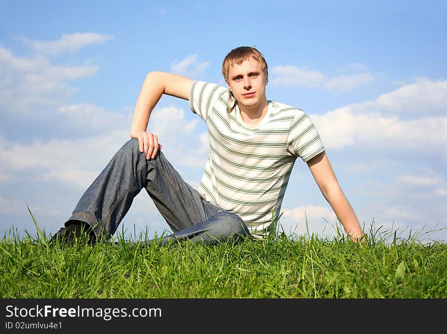 Young handsome man siting on summer lawn, hand on knee, looking at camera