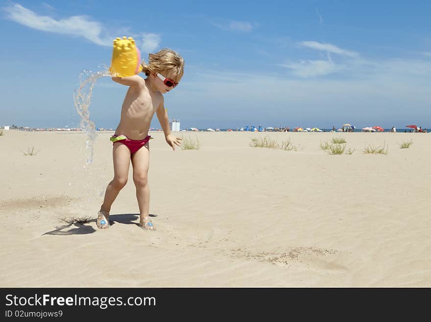 Small blond girl playing and splashing water in the beach on a summer day. Small blond girl playing and splashing water in the beach on a summer day