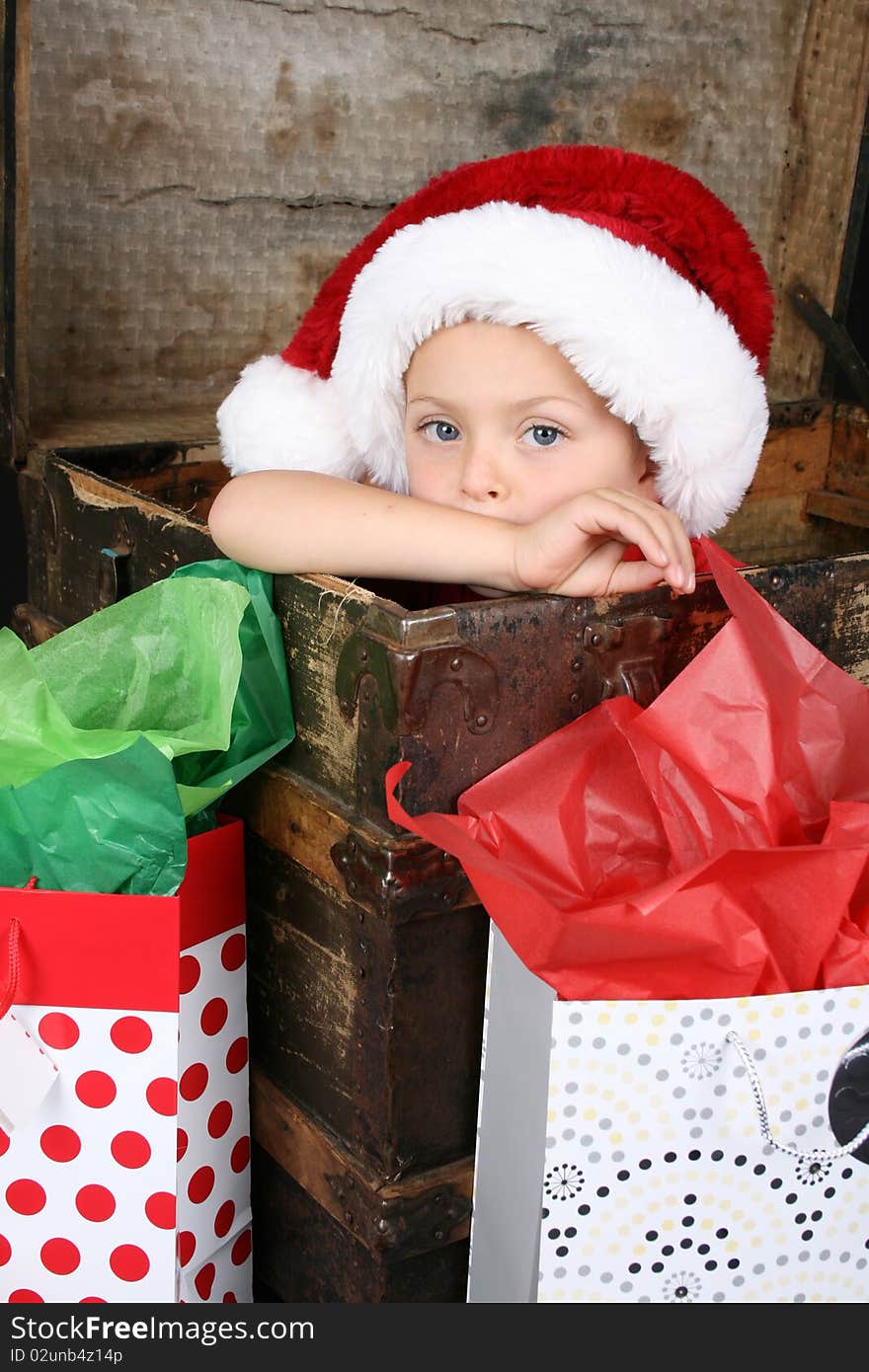 Serious boy sitting inside an antique trunk wearing a christmas hat. Serious boy sitting inside an antique trunk wearing a christmas hat