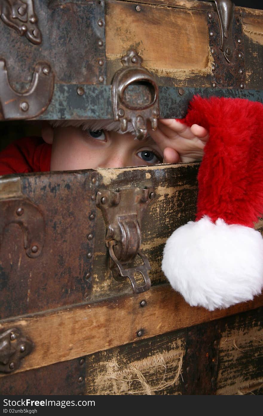 Serious boy with a christmas hat peeping from inside an antique trunk. Serious boy with a christmas hat peeping from inside an antique trunk