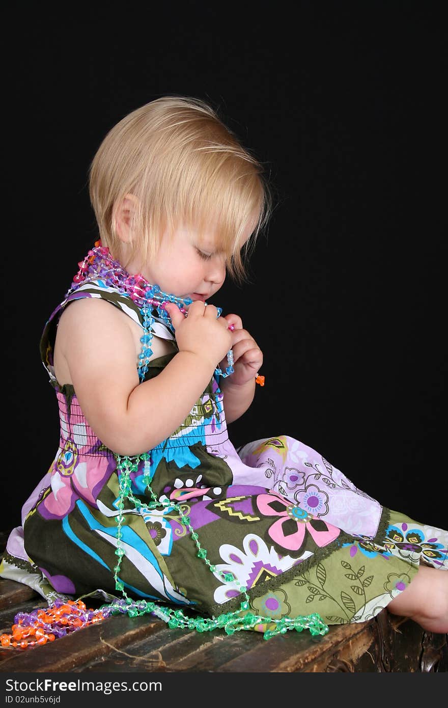 Beautiful blond toddler sitting on an antique trunk playing with beads. Beautiful blond toddler sitting on an antique trunk playing with beads