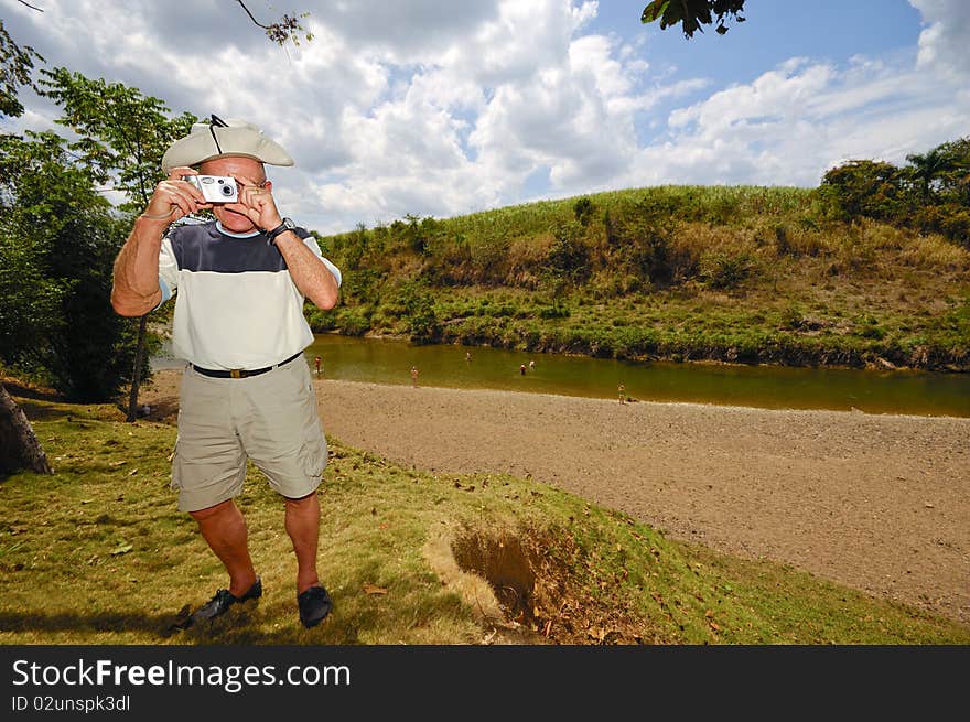 A turist is standing in green nature. The man is a senior and is holding a camera. Dominican Republic. A turist is standing in green nature. The man is a senior and is holding a camera. Dominican Republic.