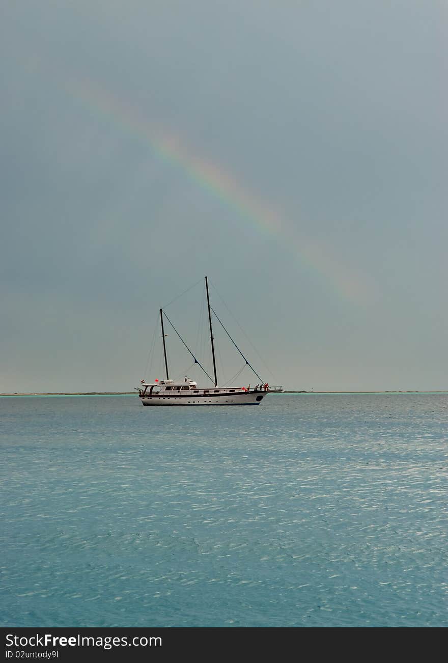 Sailing boat on a flat sea with a rainbow overhead. Sailing boat on a flat sea with a rainbow overhead