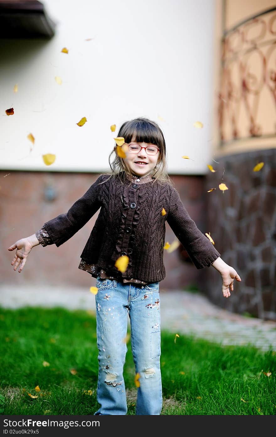 Adorable little girl plays with yellow leaves in the yard