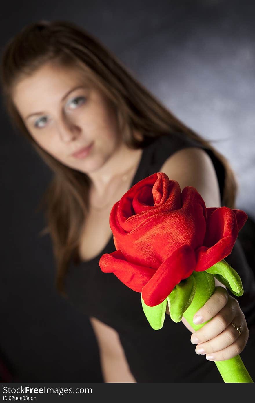 Beautiful girl giving/holding a huge plush rose isolated on black. Beautiful girl giving/holding a huge plush rose isolated on black