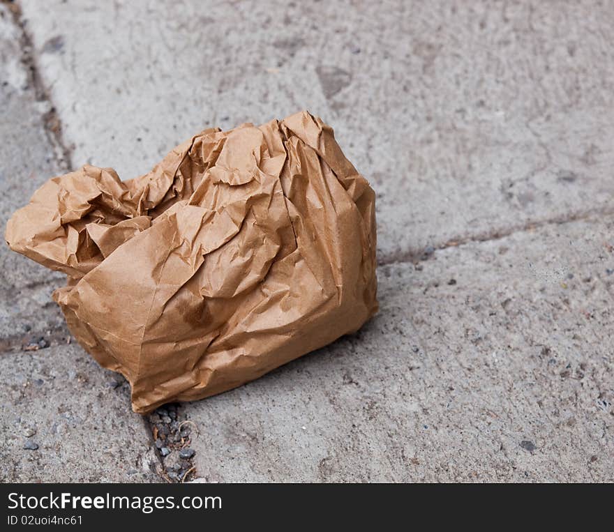 Crumpled brown paper bag discarded on a sidewalk. Crumpled brown paper bag discarded on a sidewalk