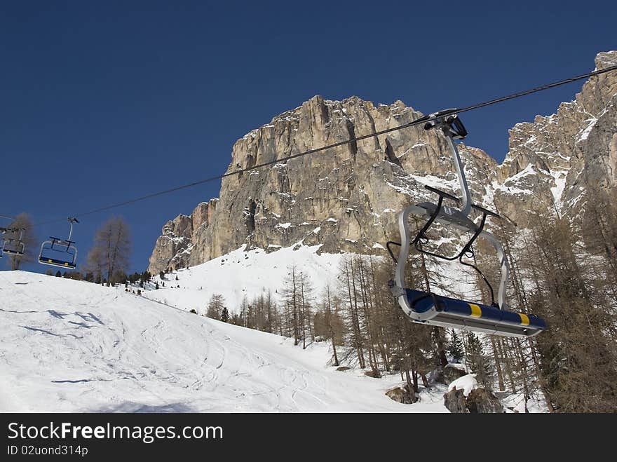 Empty chair lift in a skiing resort with mountains and blue sky in the background. Val gardena, Dolomites, Italy. Empty chair lift in a skiing resort with mountains and blue sky in the background. Val gardena, Dolomites, Italy.