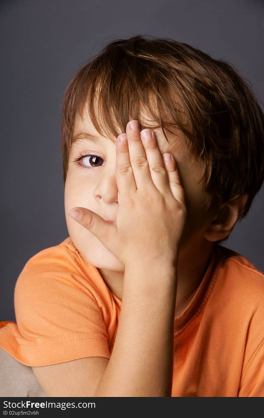 Portrait of cute little boy playing hide-and-seek, studio shot