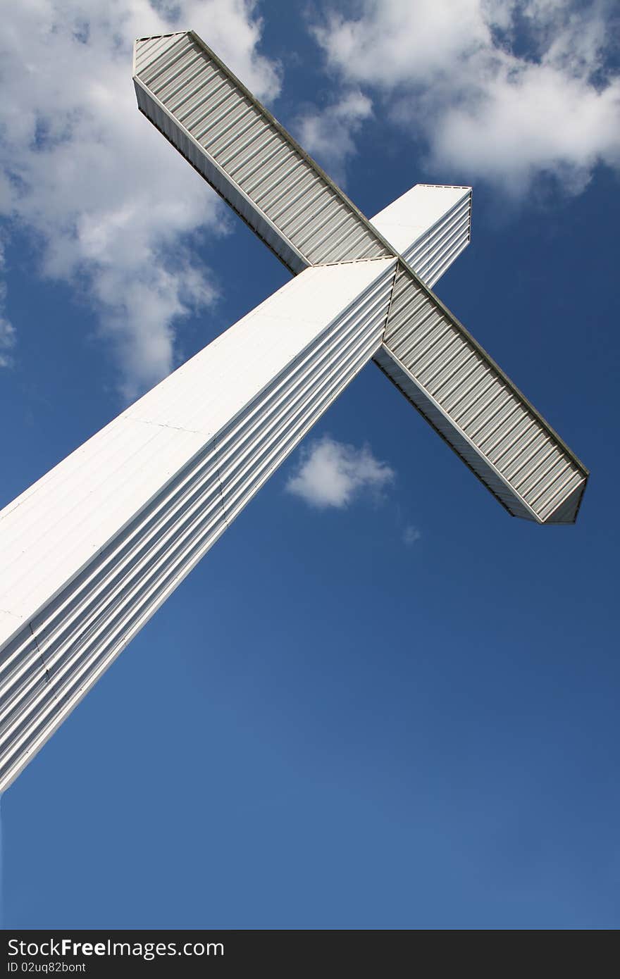 A massive modern cross slants against a cloudy blue sky. A massive modern cross slants against a cloudy blue sky.