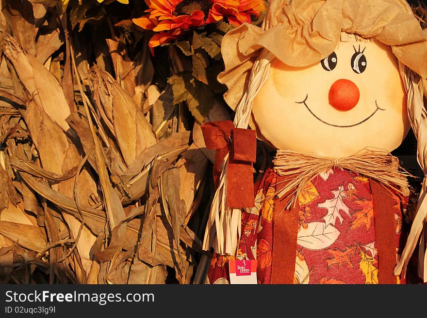 A sweet scarecrow sits next to corn husks. A sweet scarecrow sits next to corn husks.