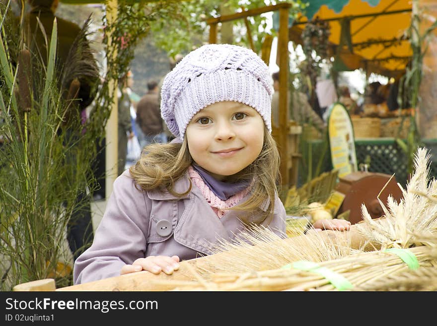 The girl in a violet raincoat and a cap costs near a cart with wheat crop. The girl in a violet raincoat and a cap costs near a cart with wheat crop