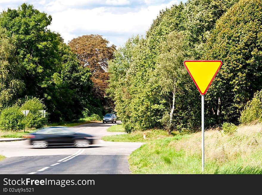 Yield sign near crossroad and rushing car