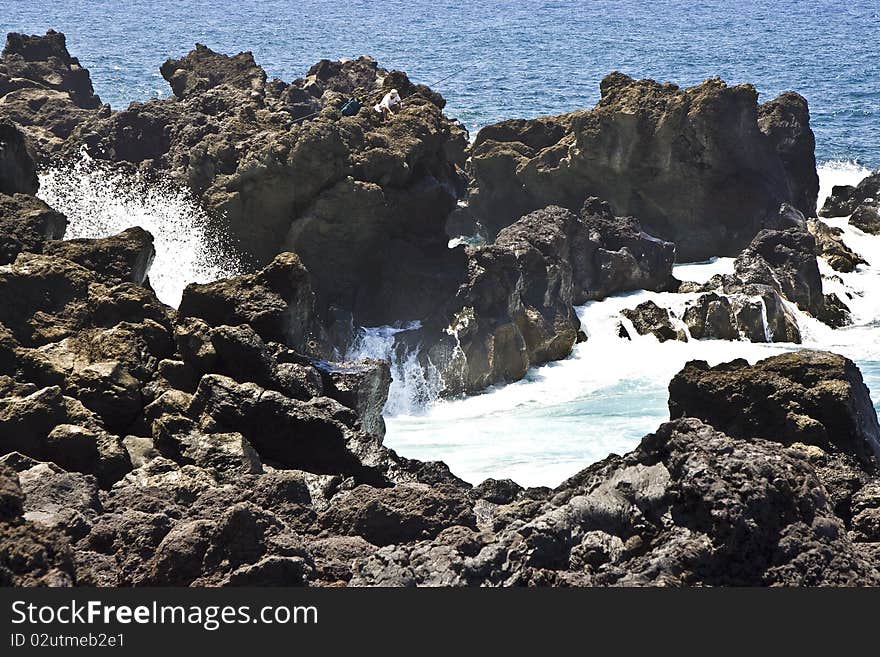 Angler on a cliff with rod in stormy sea