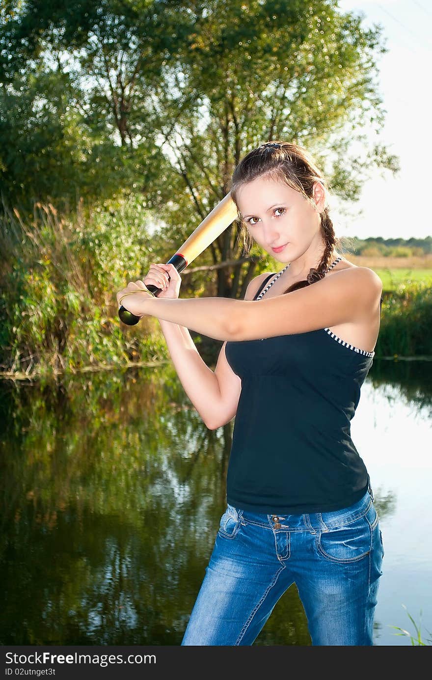 Beautiful girl with the bat against the backdrop of the river and trees in the summer. Beautiful girl with the bat against the backdrop of the river and trees in the summer.