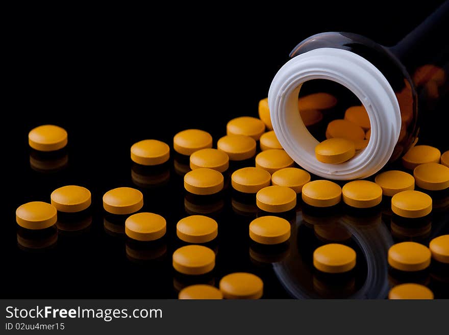 Yellow pills and a bottle on a black background