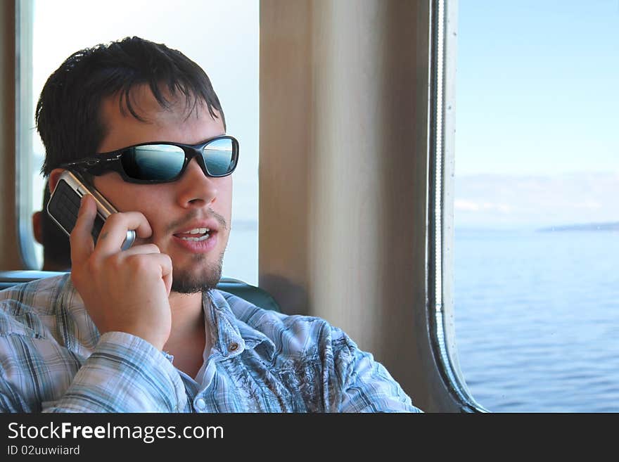 Cool guy with sunglasses talks on cell phone while commuting on a ferry. Cool guy with sunglasses talks on cell phone while commuting on a ferry