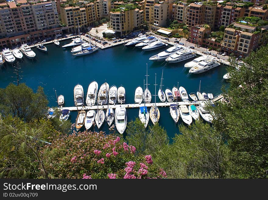 Yachts moored in a sunny marina in Monaco with surrounded by buildings.