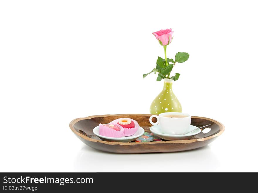 A wooden colorful tray with coffee and petit four and a rose isolated over white. A wooden colorful tray with coffee and petit four and a rose isolated over white