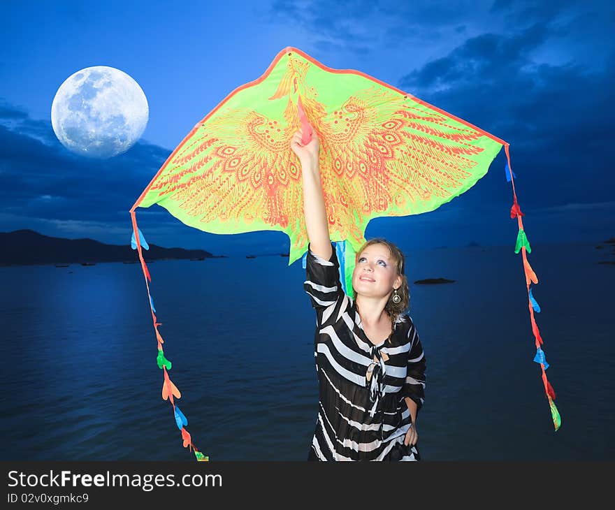 Beautiful woman with kite on the beach under moon