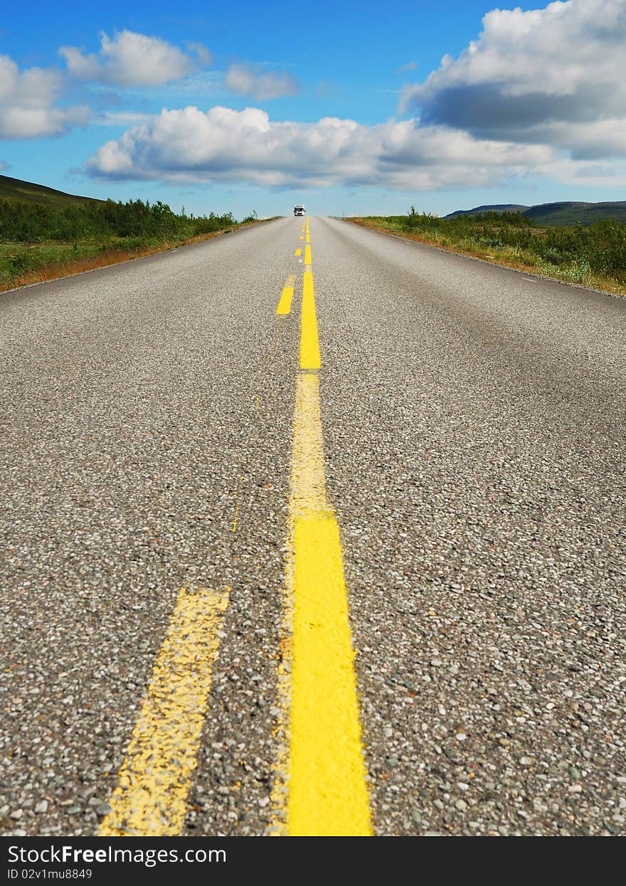 Asphalt road with yellow line is running away. Norwegian highway is photographed with diminishing perspective. Asphalt road with yellow line is running away. Norwegian highway is photographed with diminishing perspective.