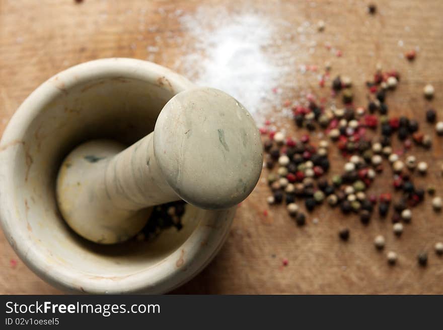 A still life with mortar and pestle with pepper near them on a wooden hardboard. A still life with mortar and pestle with pepper near them on a wooden hardboard