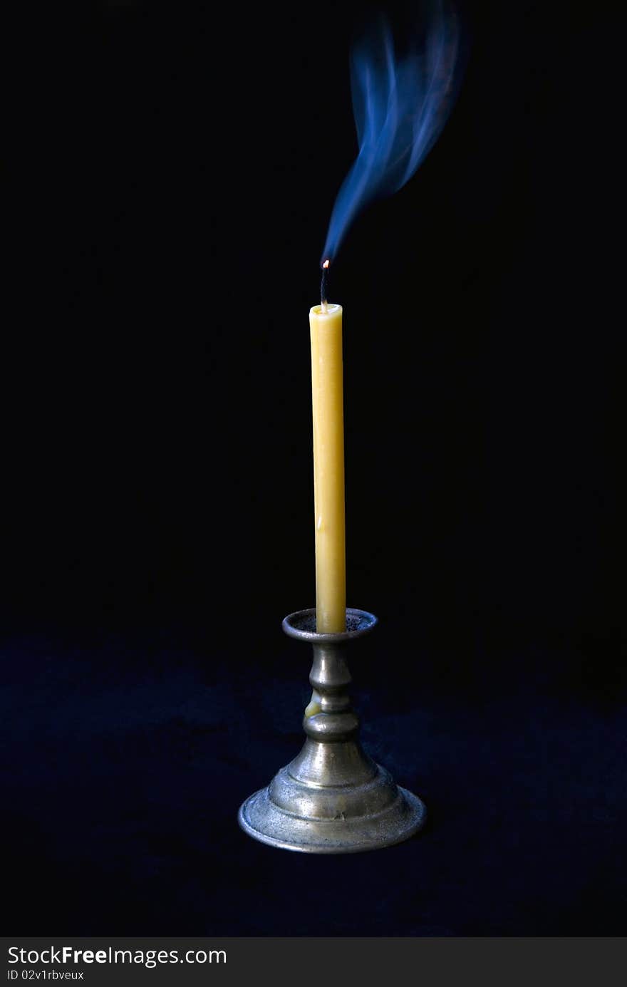 The extinct candle in a candlestick smokes on a black background. The extinct candle in a candlestick smokes on a black background.