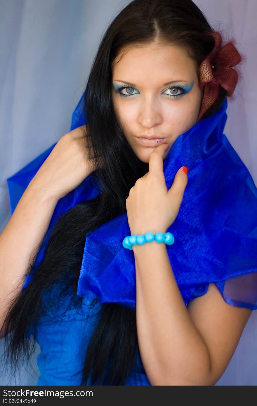 Beautiful girl with blue eyes and dark hair. Girl dressed in a blue cloth, like a dress. In her hair - burgundy flower. Beautiful girl with blue eyes and dark hair. Girl dressed in a blue cloth, like a dress. In her hair - burgundy flower