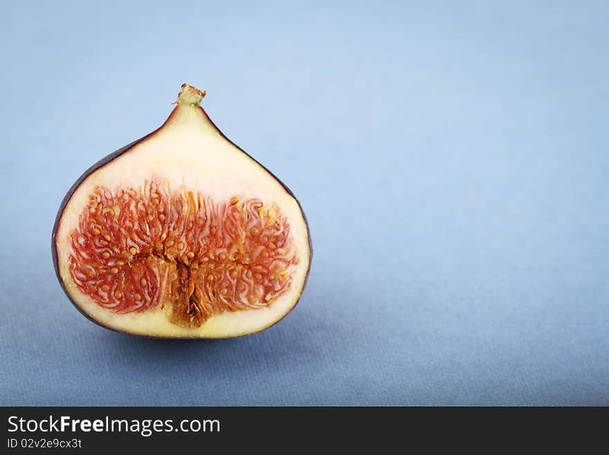 One halved fig on the blue background. One halved fig on the blue background