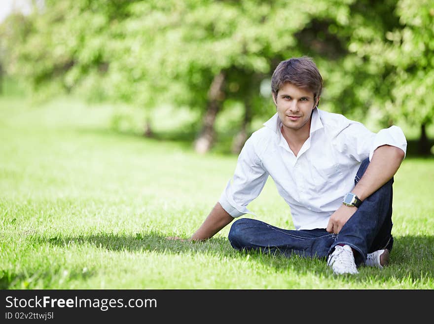 A young handsome man sits on the lawn. A young handsome man sits on the lawn