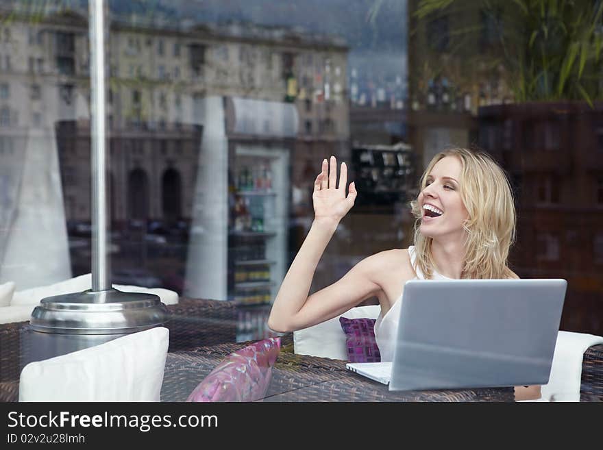 Attractive girl with a laptop waving to someone. Attractive girl with a laptop waving to someone