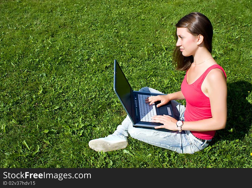 Young pretty woman with laptop sitting on green lawn in a park. Young pretty woman with laptop sitting on green lawn in a park