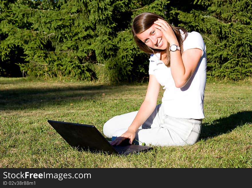 Smiling girl with a laptop on a lawn