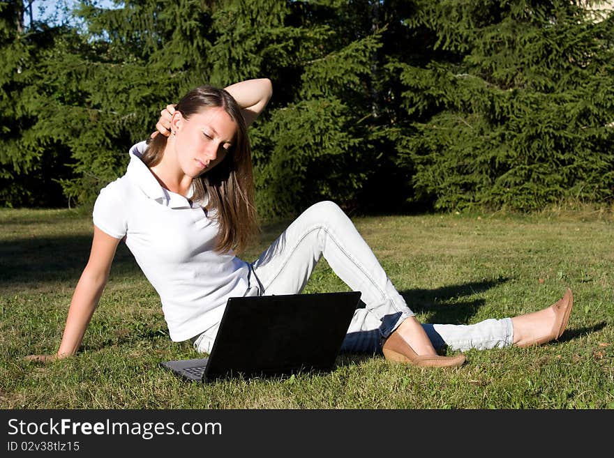 Smiling girl with a laptop on a lawn