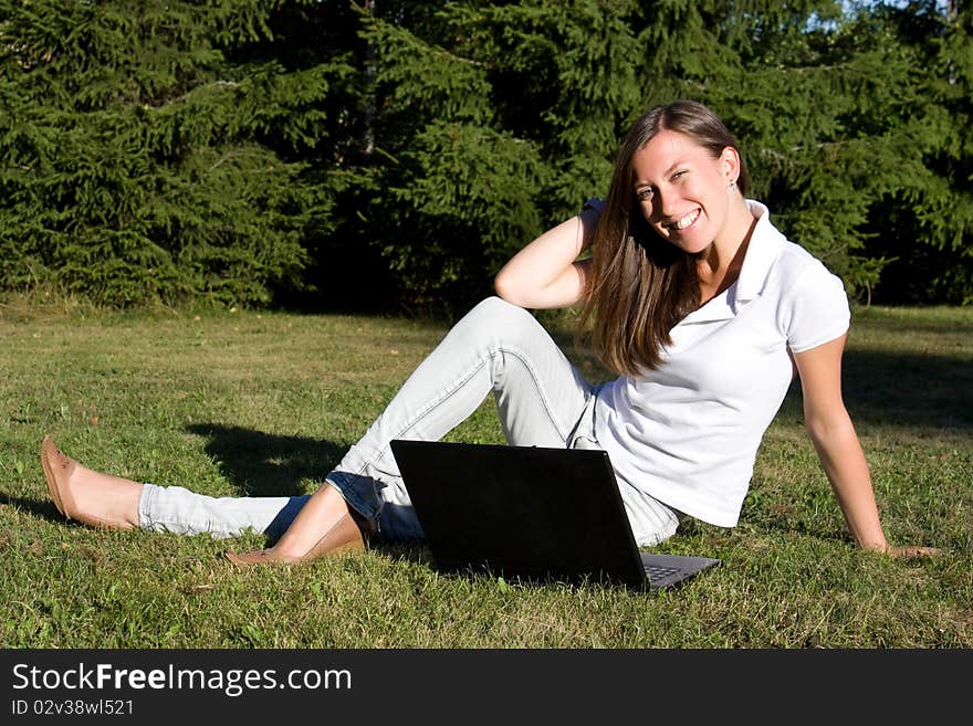 Smiling girl with a laptop on a lawn