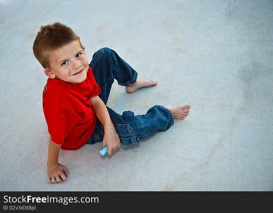 Cute young boy playing with sidewalk chalk.