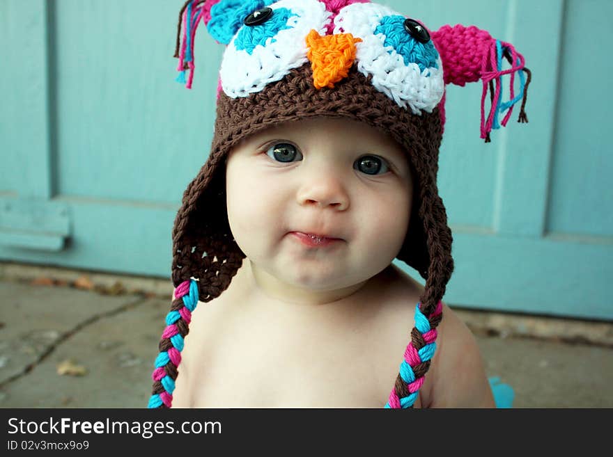 A cute baby girl sitting surrounded with a blue frilly skirt and hat.