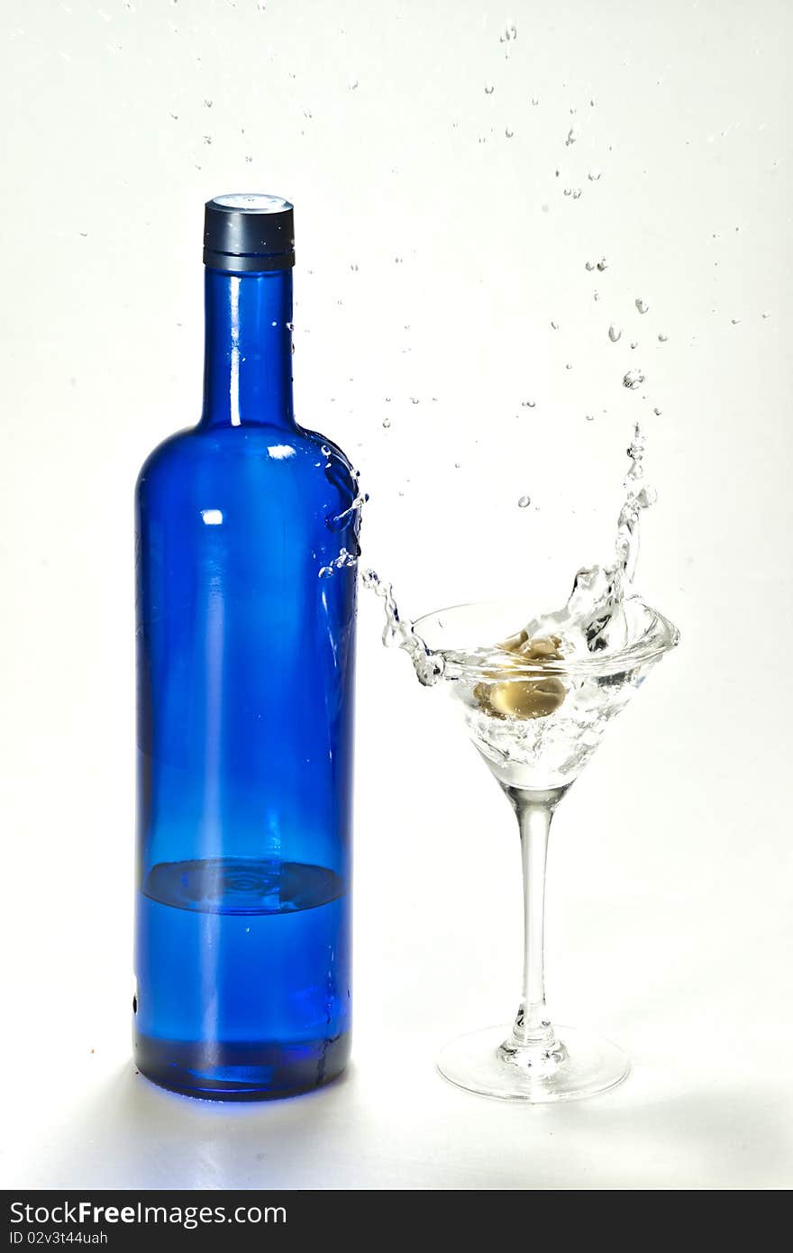 A splash of martini made by olive with a blue bottle of vodka