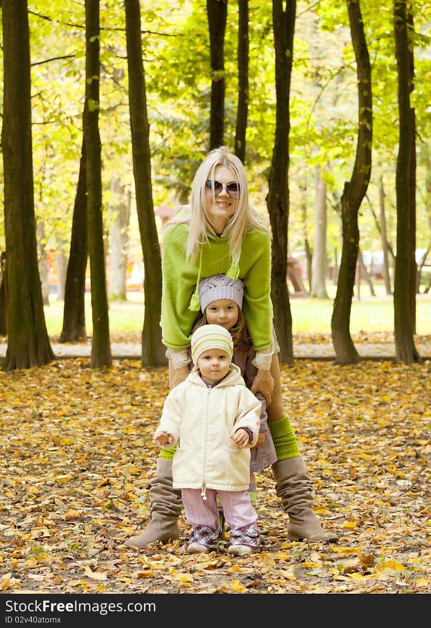 The woman with children costs nearby and smile in the autumn in park. The woman with children costs nearby and smile in the autumn in park