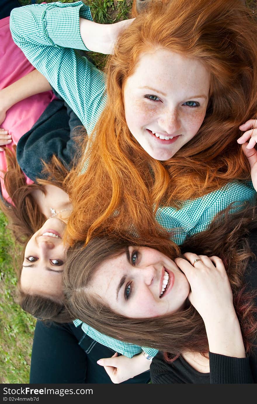 Three different girls are sitting on the grass smiling and hugging in a spring daytime. Three different girls are sitting on the grass smiling and hugging in a spring daytime