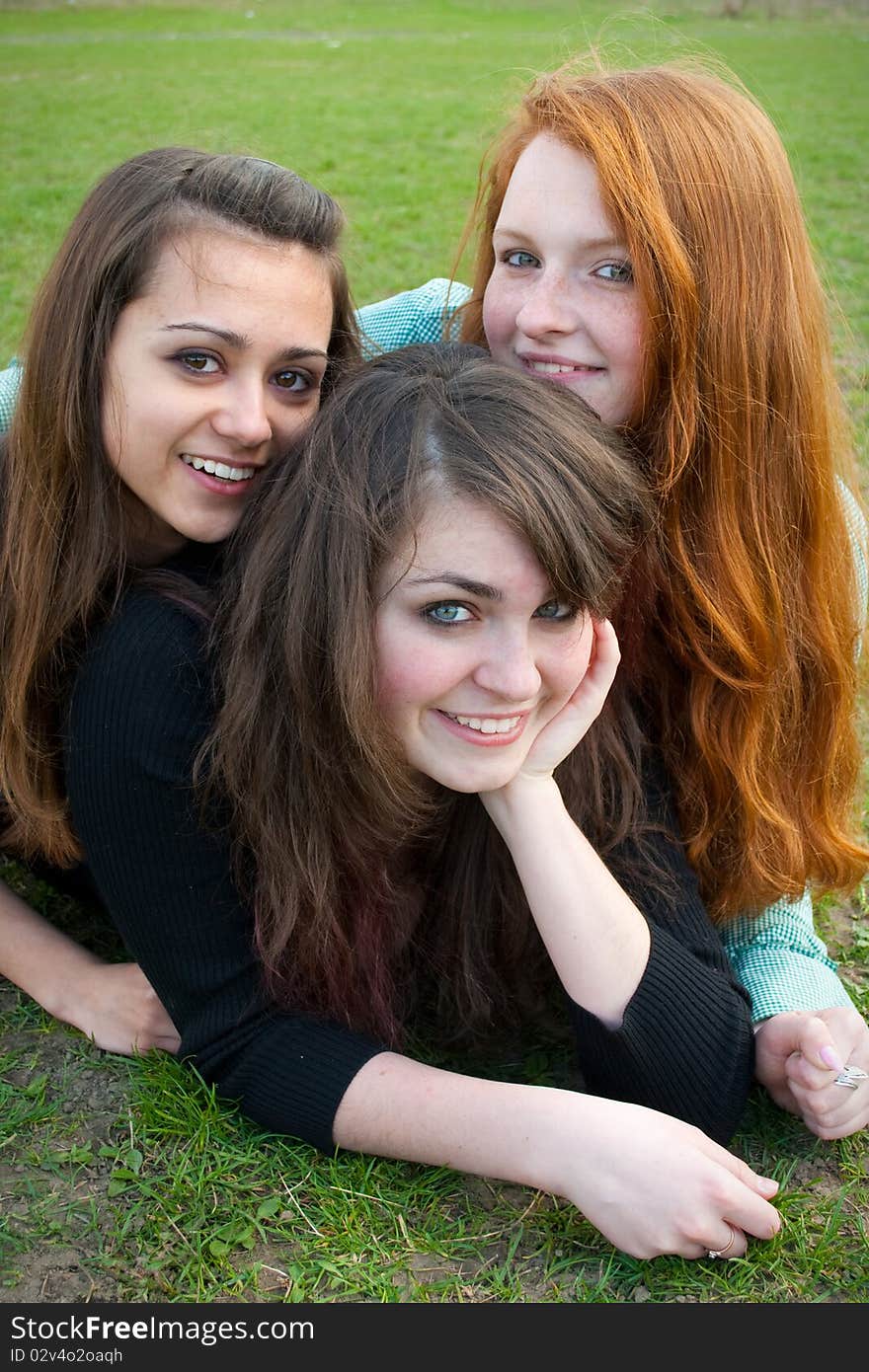 Three different girls are sitting on the grass smiling and hugging in a spring daytime. Three different girls are sitting on the grass smiling and hugging in a spring daytime