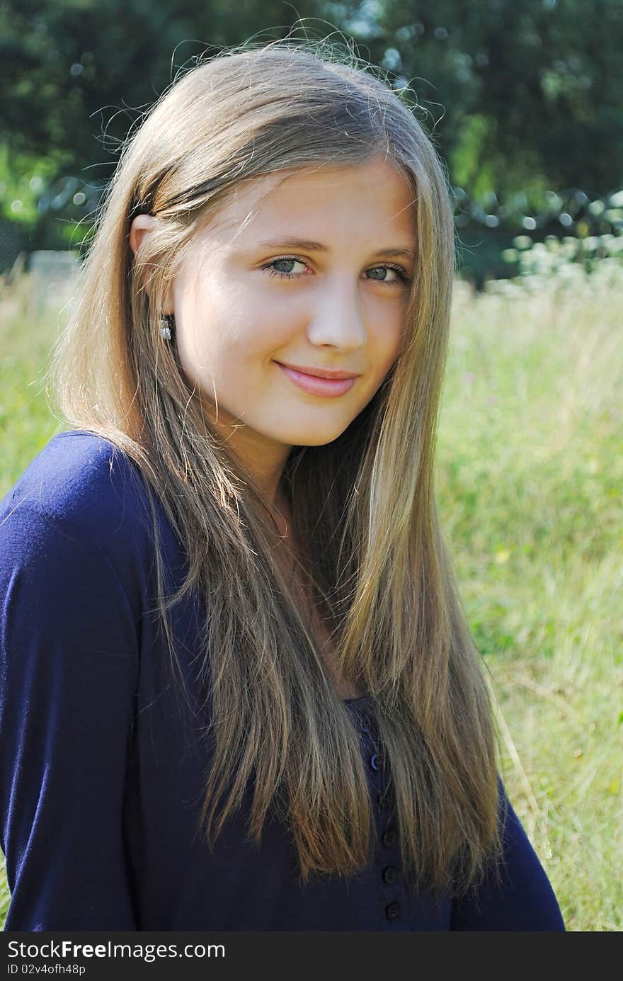 Beautiful smiling young pretty girl is seating in the park and looking at you. Beautiful smiling young pretty girl is seating in the park and looking at you