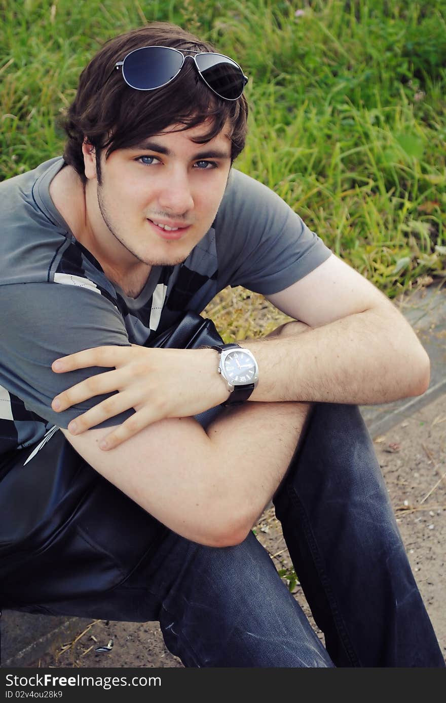 Beutiful young boy is seating on the grass and looking at you