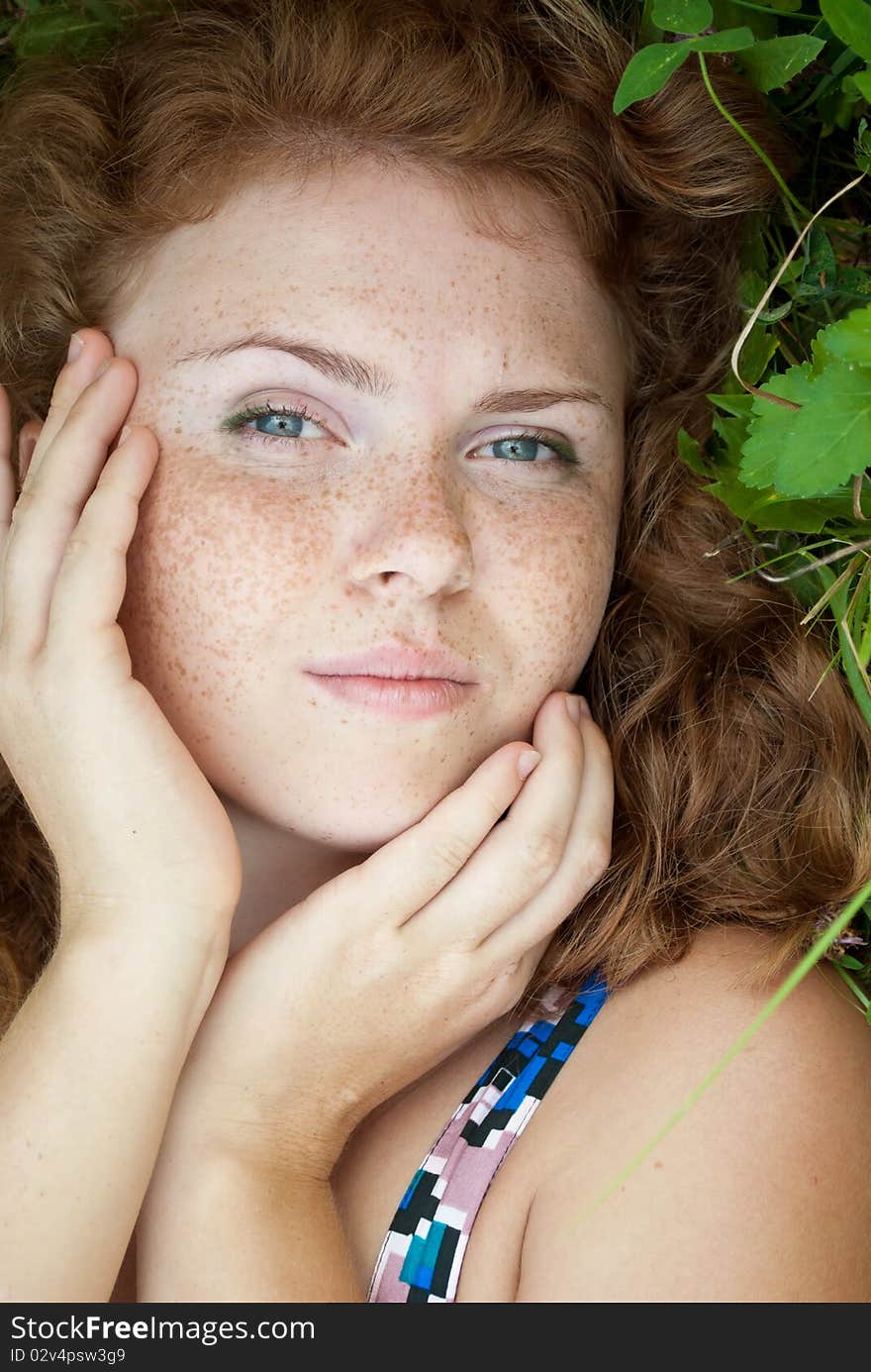 Beautiful ginger girl is lying in the green grass and smiling