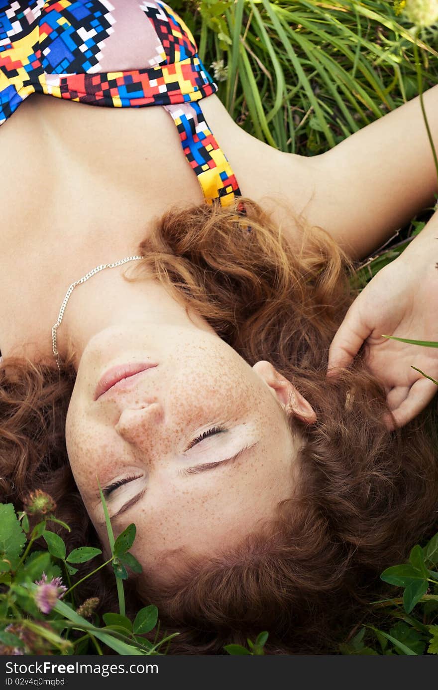 Beautiful ginger girl is lying in the green grass with closed eyes