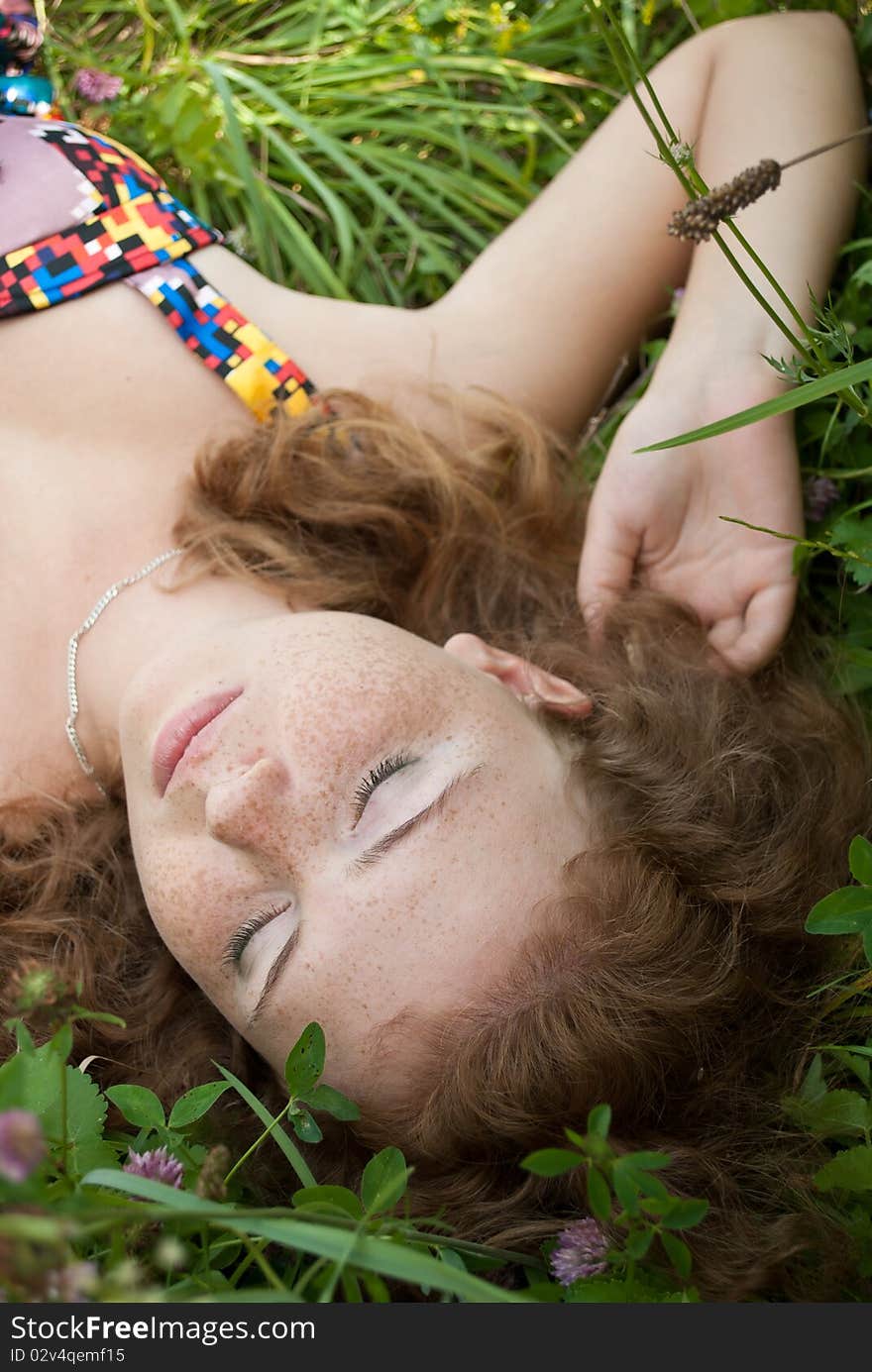 Beautiful ginger girl is lying in the green grass with closed eyes