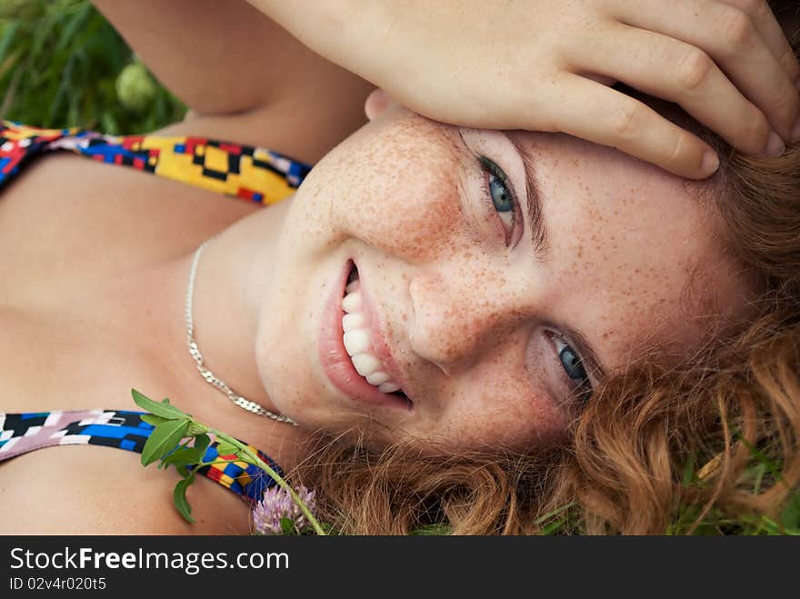 Beautiful ginger girl is lying in the green grass and smyling