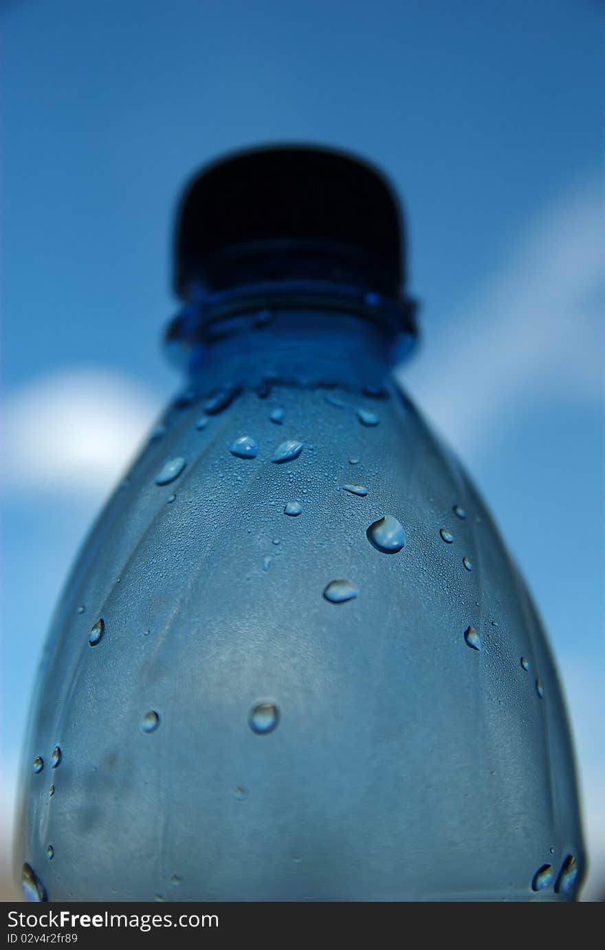 Bottle with drops of water with blue sky with some clouds on the background. Bottle with drops of water with blue sky with some clouds on the background.