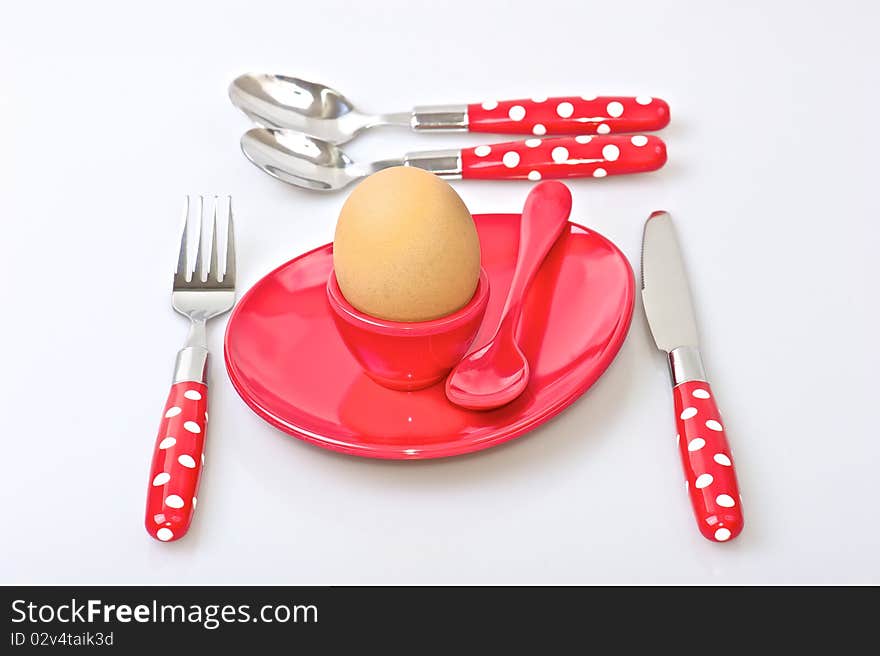 Table set for breakfast with red and white polka dot cutlery, brown egg and red egg cup and  saucer